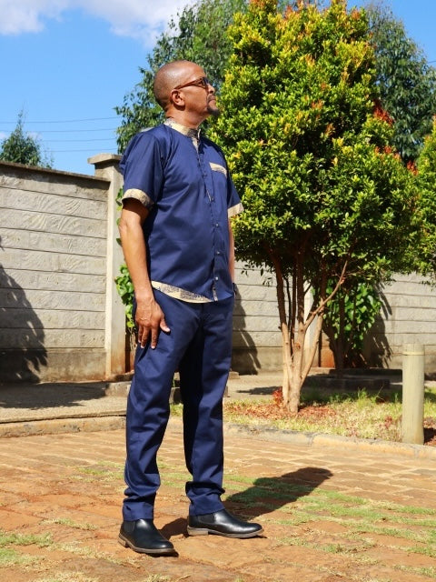 Man wearing a navy blue short-sleeve shirt and trousers set with traditional African print accents on collar and cuffs.