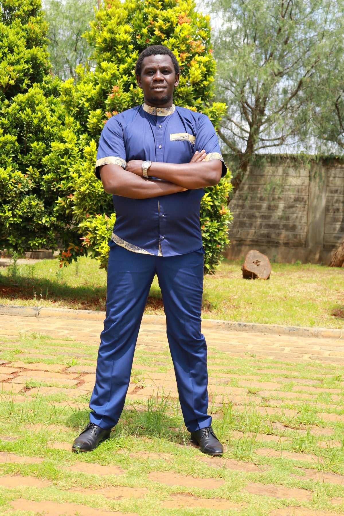 Man wearing a navy blue short-sleeve shirt and trousers set with traditional African print accents on collar and hem.
